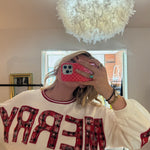 Woman wearing a cream crewneck sweatshirt with red plaid MERRY appliqué lettering, holiday style