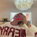Woman wearing a cream crewneck sweatshirt with red plaid MERRY appliqué lettering, holiday style