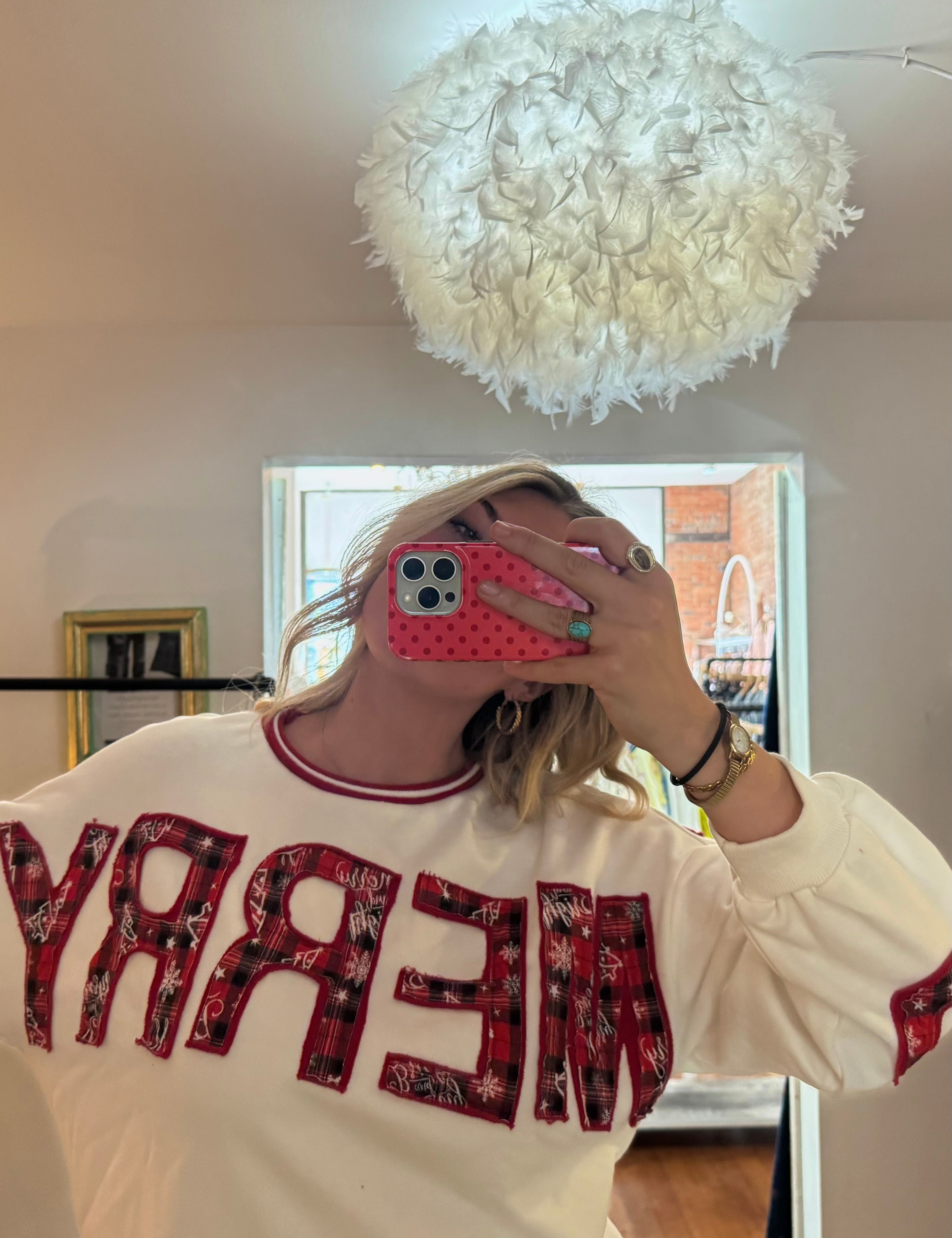 Woman wearing a cream crewneck sweatshirt with red plaid MERRY appliqué lettering, holiday style