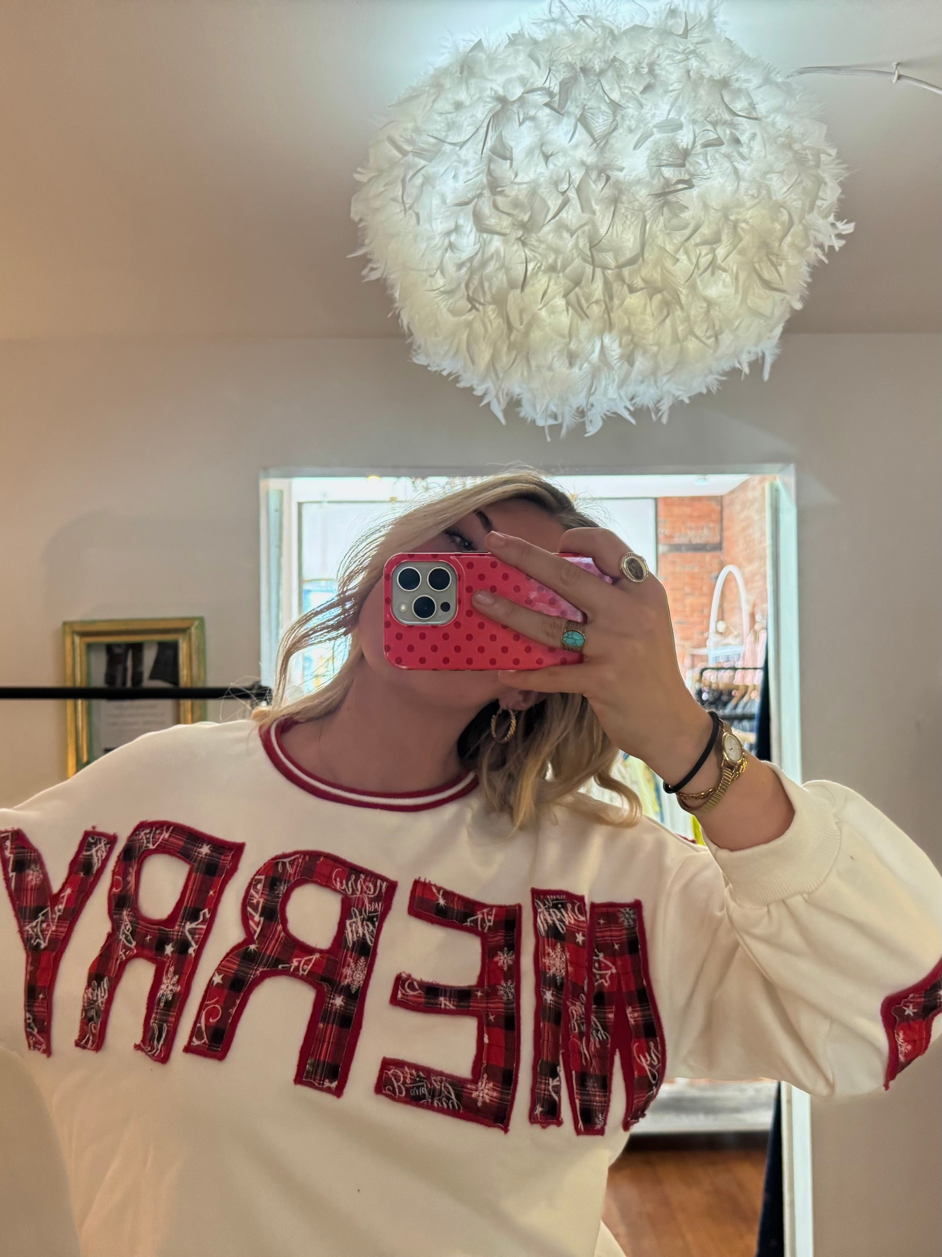 Woman wearing a cream crewneck sweatshirt with red plaid MERRY appliqué lettering, holiday style