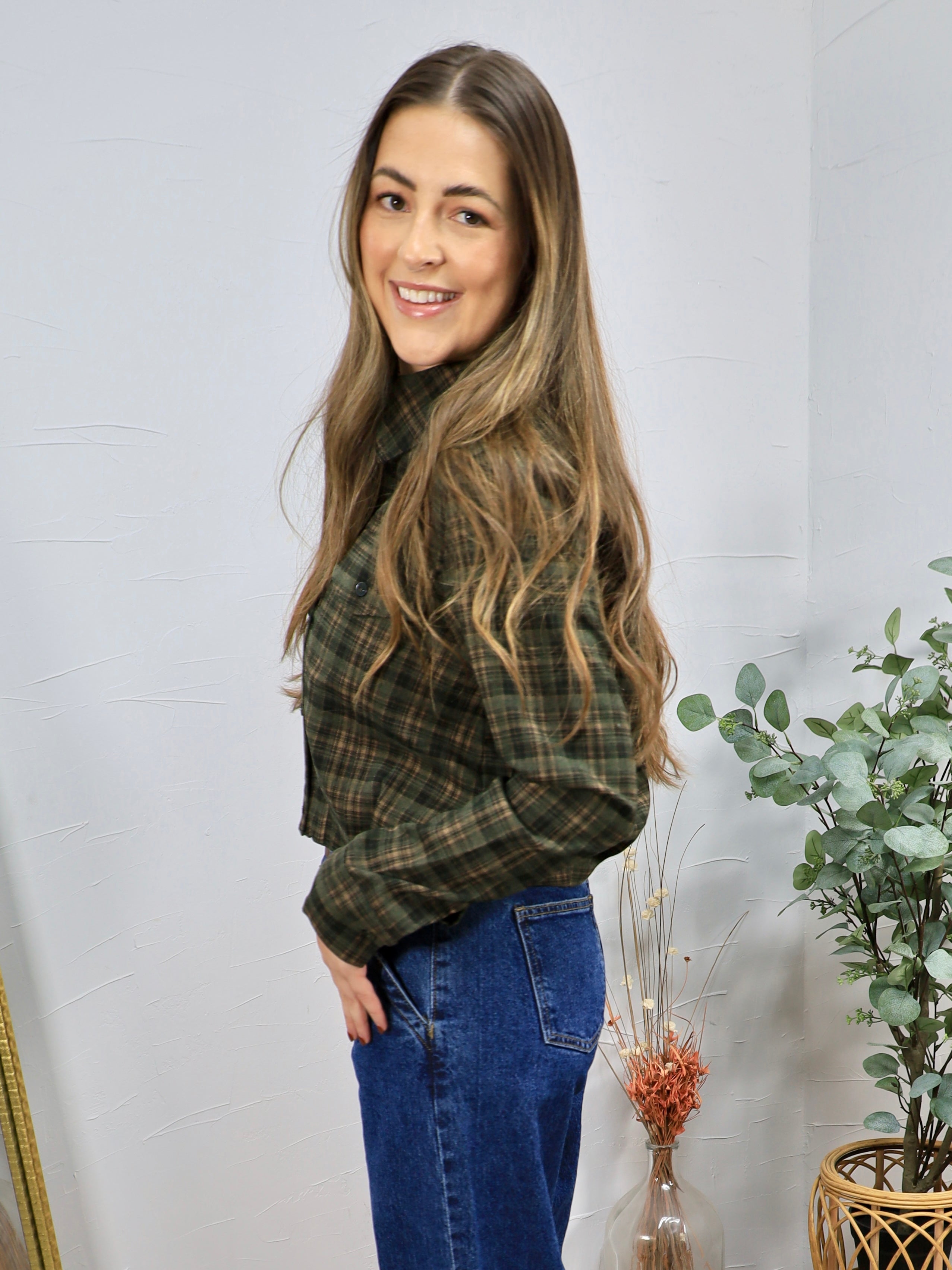Green and brown plaid cropped button-up shirt styled with blue high-waisted jeans, side profile view.