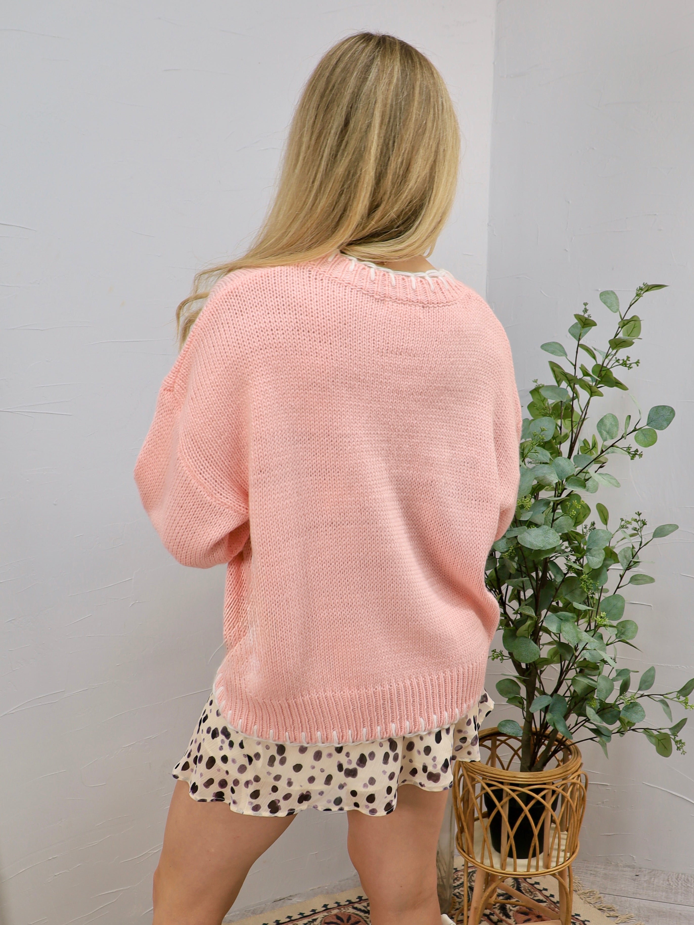 Pink oversized knit sweater styled over a spotted mini skirt, shown from the back view.