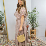 Woman wearing brown and white gingham checkered tiered midi dress with puffed sleeves, holding woven straw handbag and nude h
