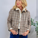 Cropped brown plaid jacket with gold buttons and dark collar, layered over cream shirt with blue jeans.