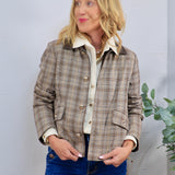 Cropped brown plaid jacket with gold buttons and dark collar, layered over cream shirt with blue jeans.