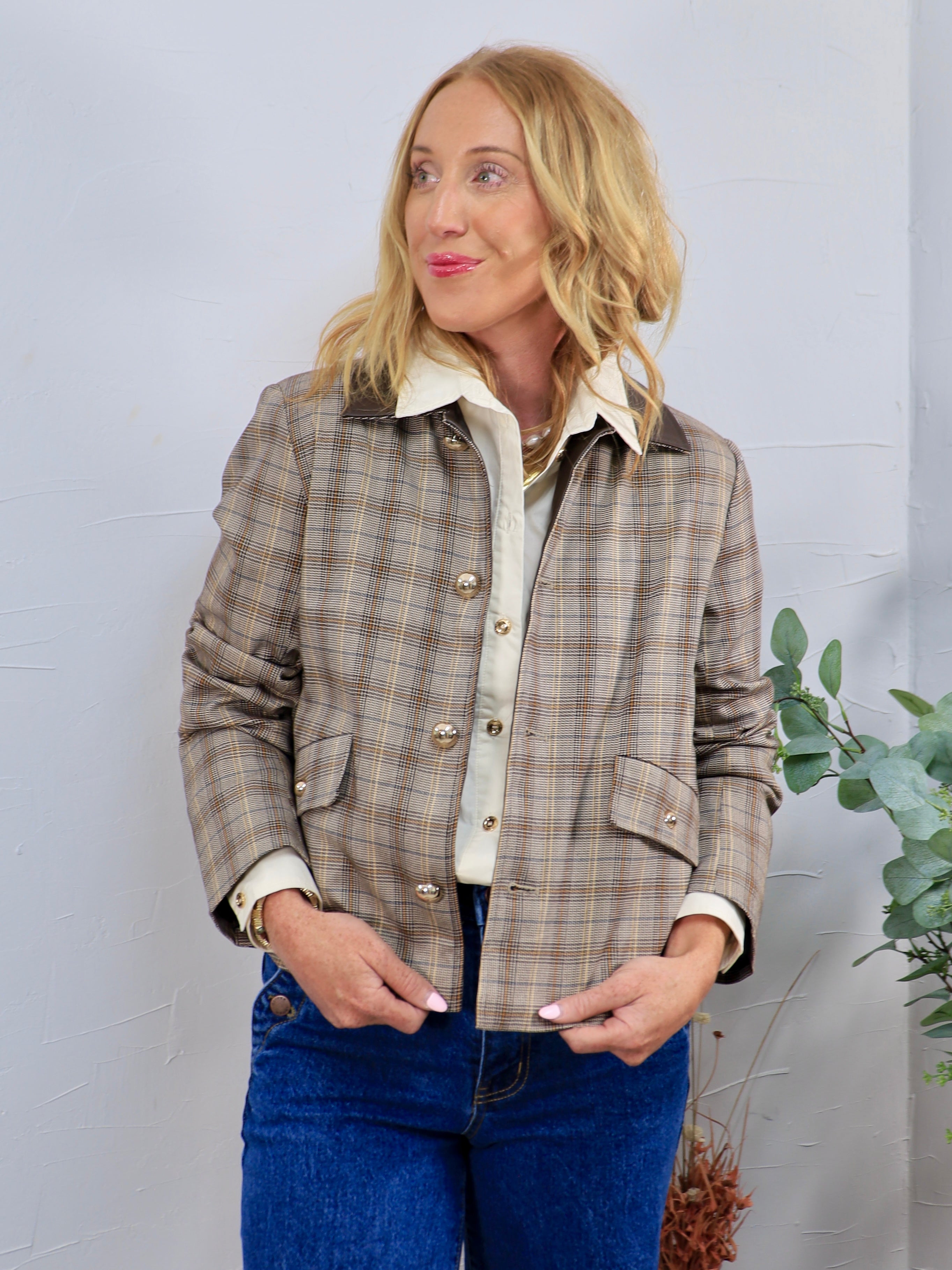 Cropped brown plaid jacket with gold buttons and dark collar, layered over cream shirt with blue jeans.
