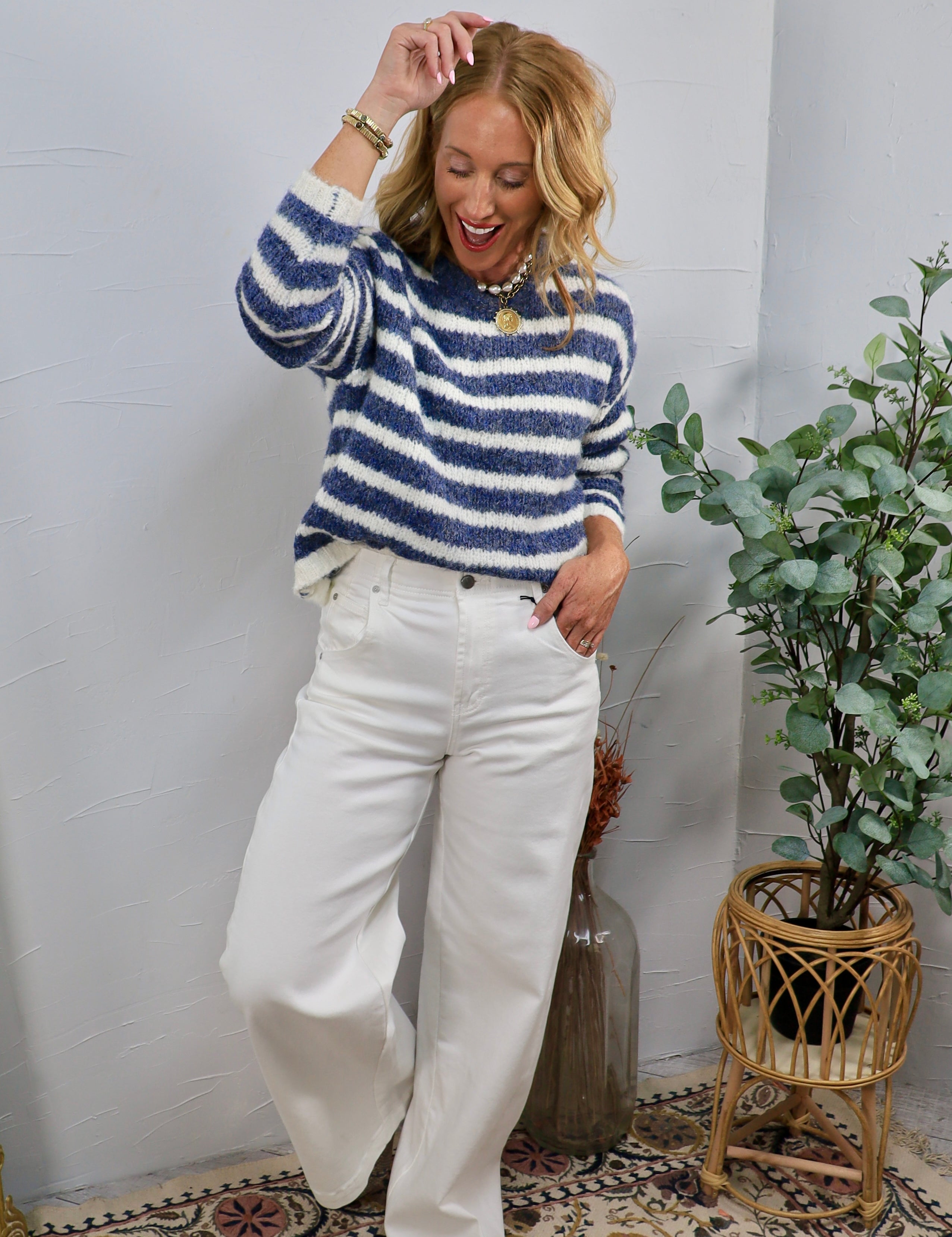 Woman wearing a blue and white fuzzy striped crewneck sweater with wide-leg white jeans