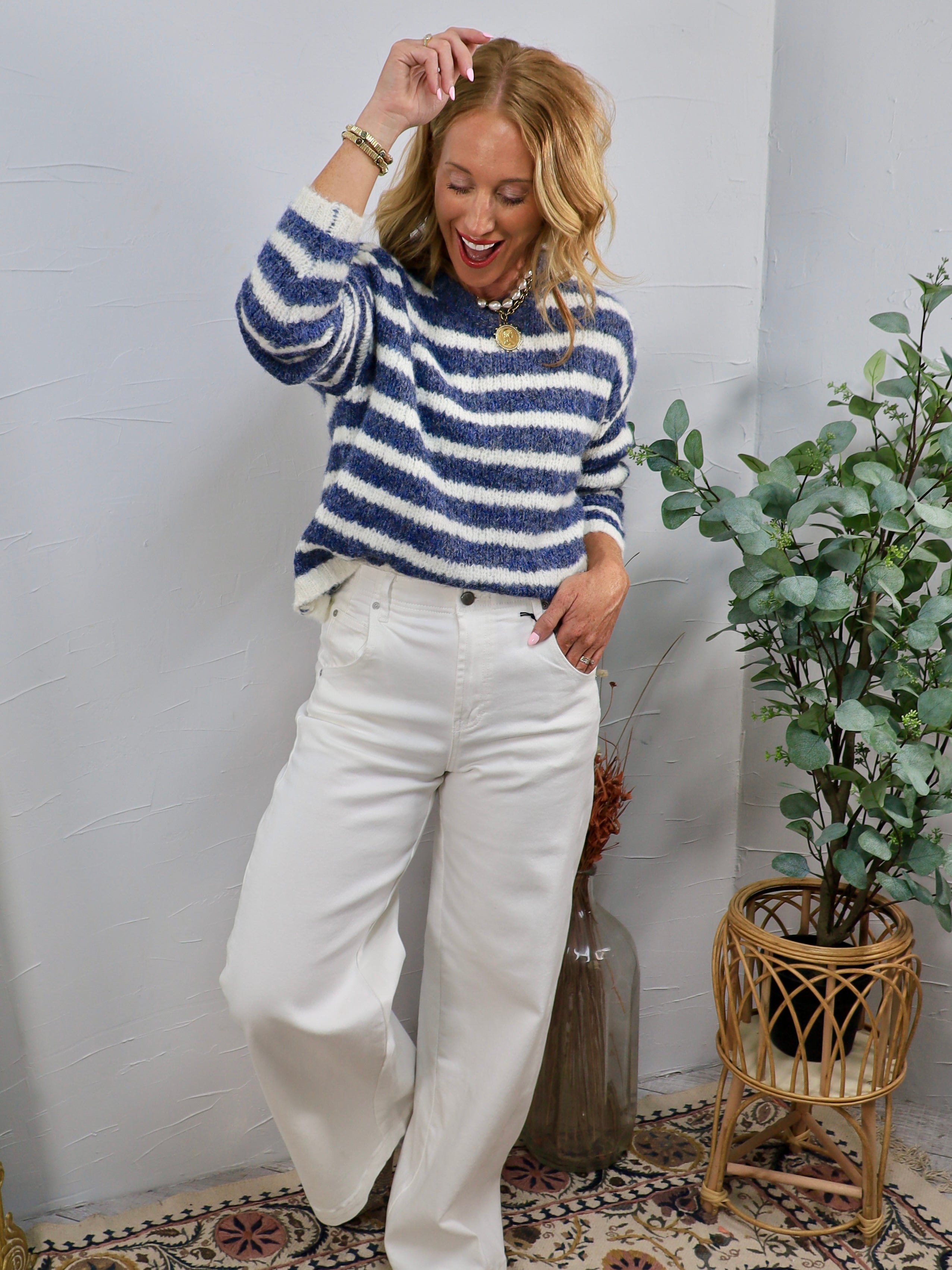 Woman wearing a blue and white fuzzy striped crewneck sweater with wide-leg white jeans