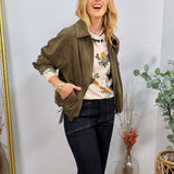 Olive green ruched suede zip-up jacket styled open over a floral sweater and dark flare jeans.