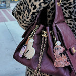 Burgundy quilted Chanel handbag with novelty keychains including a swan, nail polish, and dog charm.