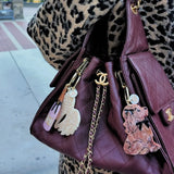 Burgundy quilted Chanel handbag with novelty keychains including a swan, nail polish, and dog charm.