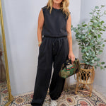 Woman wearing a dark charcoal sleeveless jumpsuit set with wide-leg jogger pants and silver sneakers