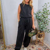 Woman wearing a dark charcoal sleeveless jumpsuit set with wide-leg jogger pants and silver sneakers