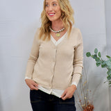 Beige ribbed cardigan layered over white top, styled with dark jeans and gold coin pearl necklace.