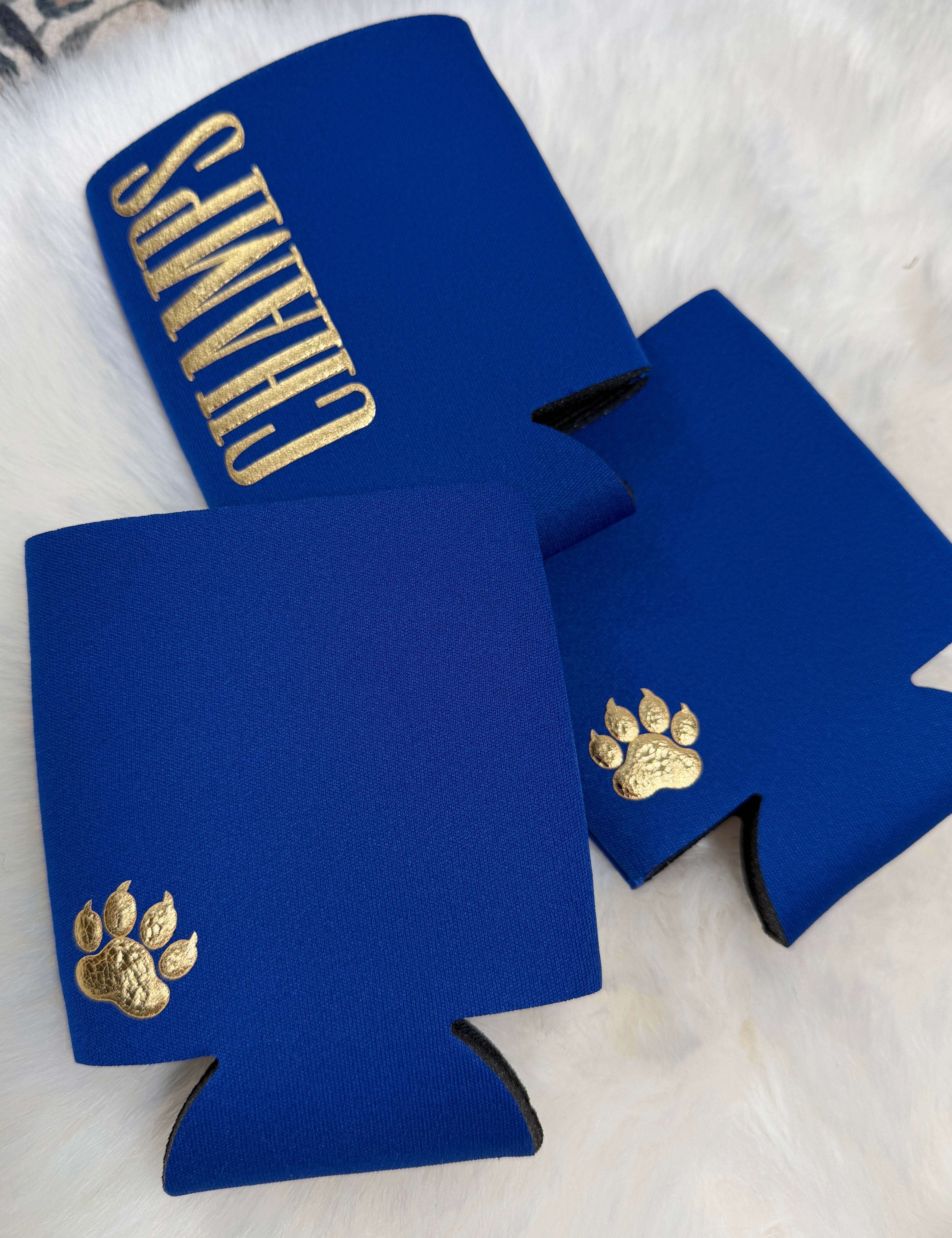 Royal blue neoprene koozies with gold embroidered paw print and "Champs" text lettering.