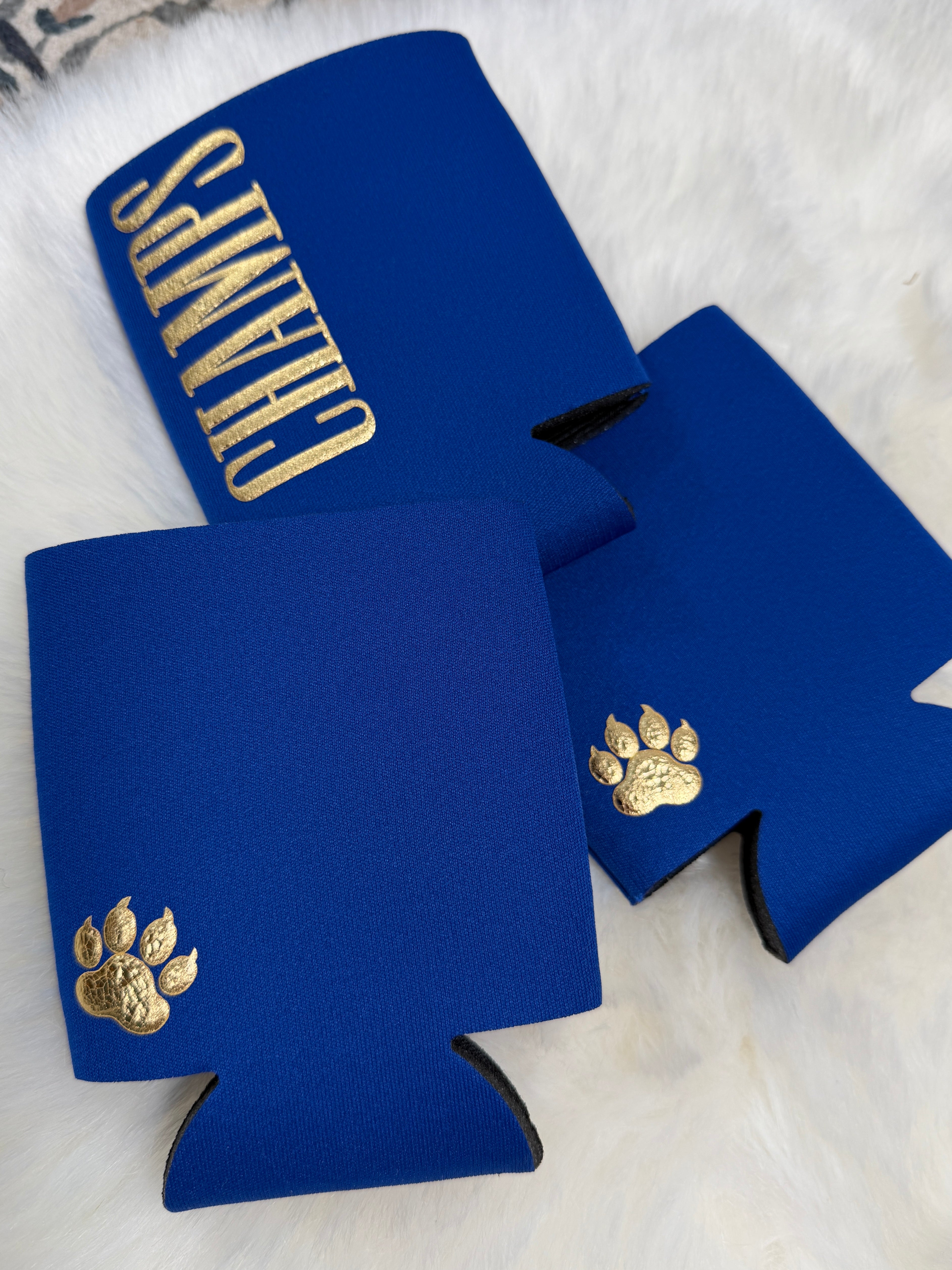 Royal blue neoprene koozies with gold embroidered paw print and "Champs" text lettering.