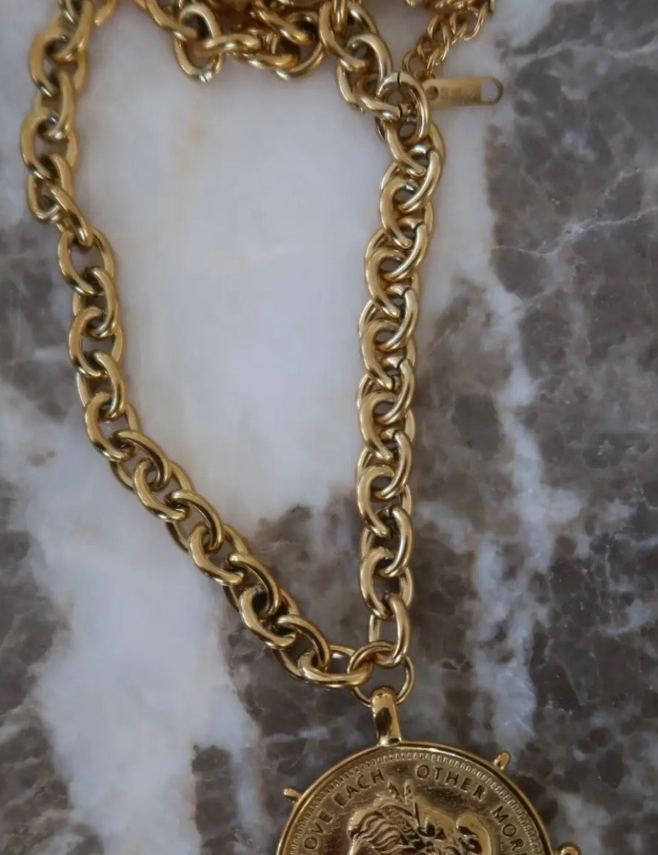 Gold chunky chain necklace with circular coin pendant engraved "Love Each Other More" on marble surface.