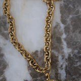 Gold chunky chain necklace with circular coin pendant engraved "Love Each Other More" on marble surface.