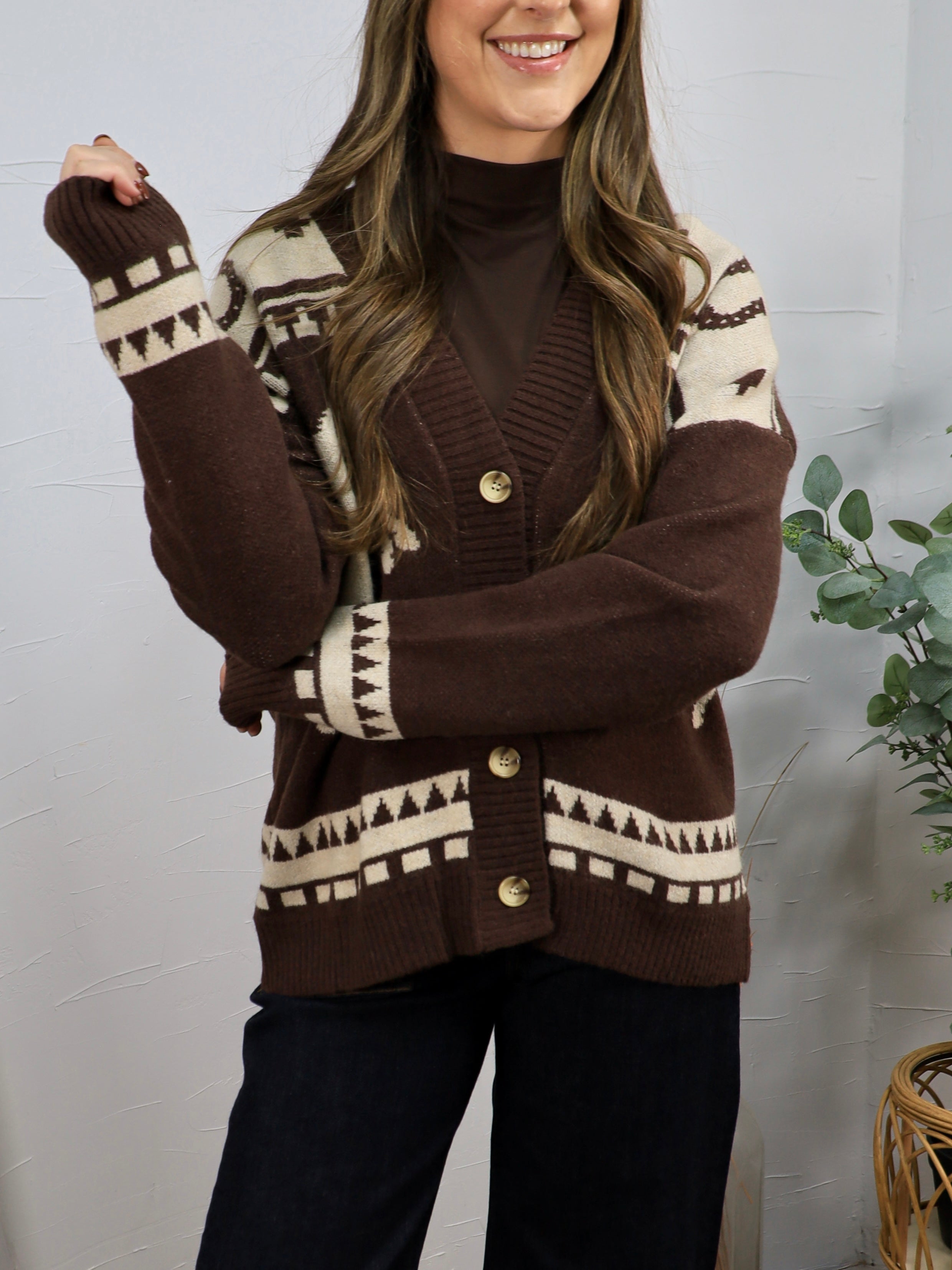 Brown and cream geometric patterned button-front cardigan layered over a brown turtleneck with black pants.