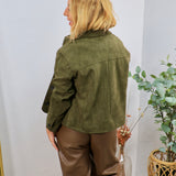 Olive green suede jacket worn from behind, styled with brown leather wide-leg trousers, button cuffs visible.