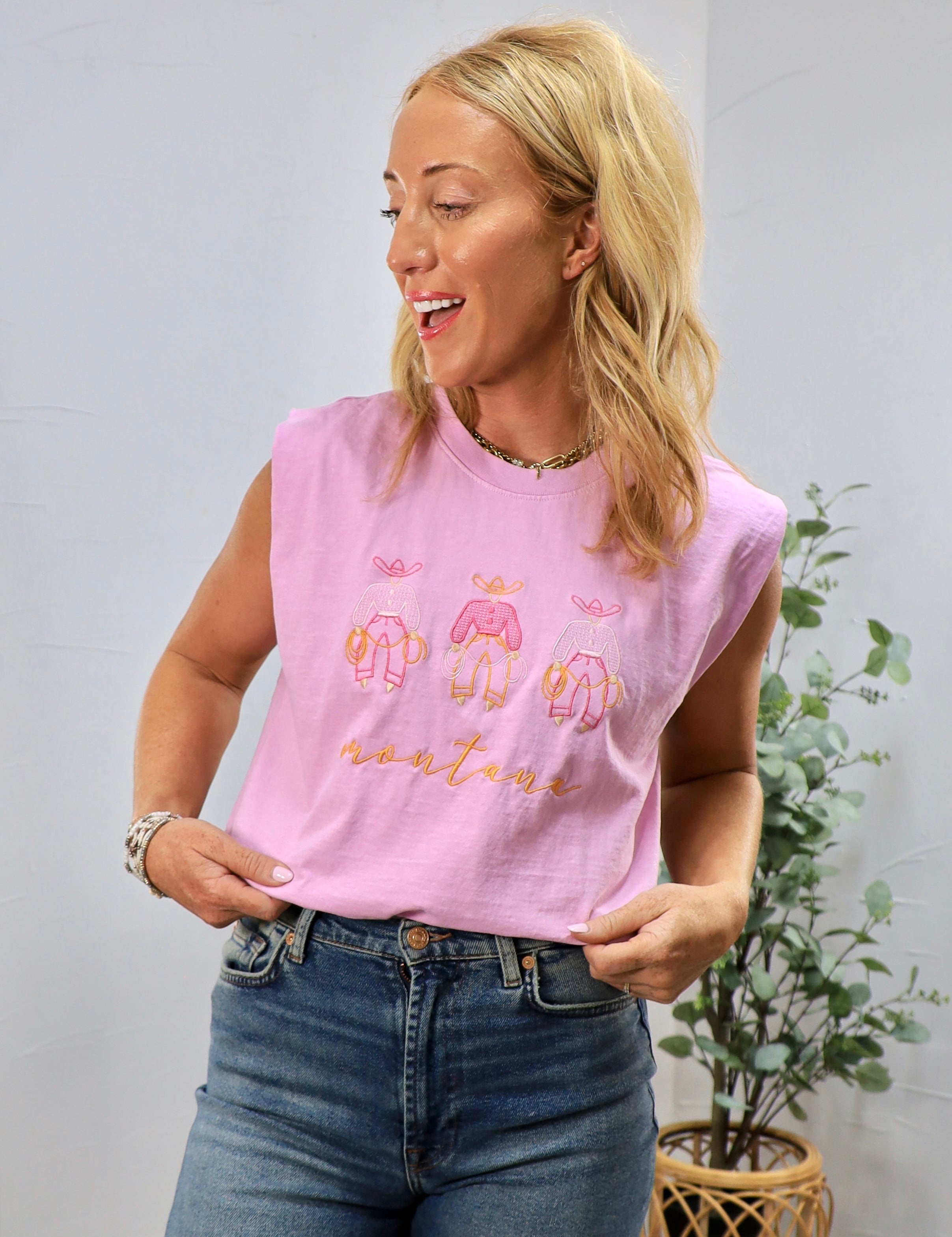 Pink sleeveless muscle tee with embroidered Montana text and cute graphics worn with jeans