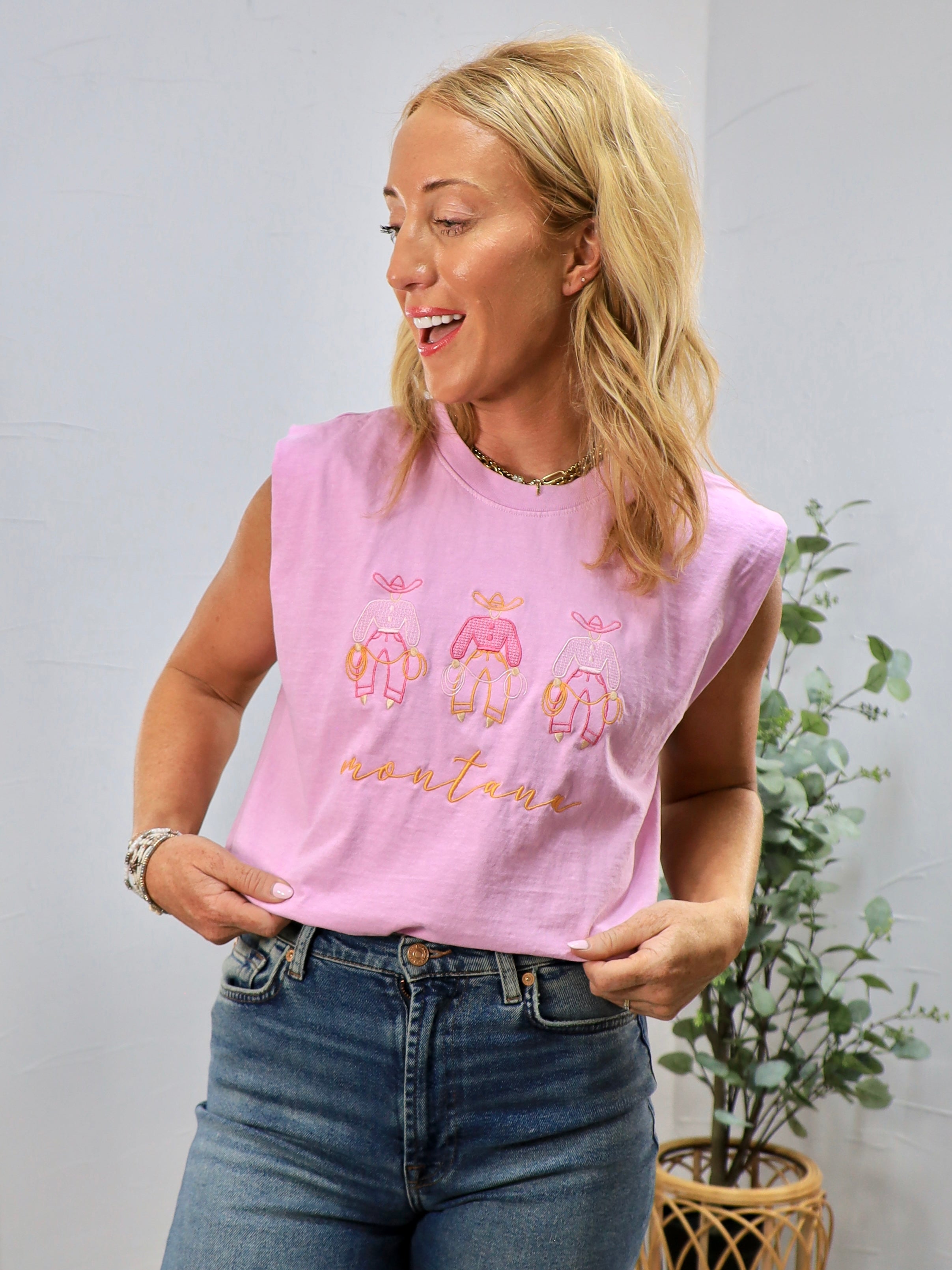 Pink sleeveless muscle tee with embroidered Montana text and cute graphics worn with jeans
