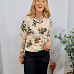 Cream floral knit sweater with colorful botanical print, styled with dark jeans and layered pearl necklace.