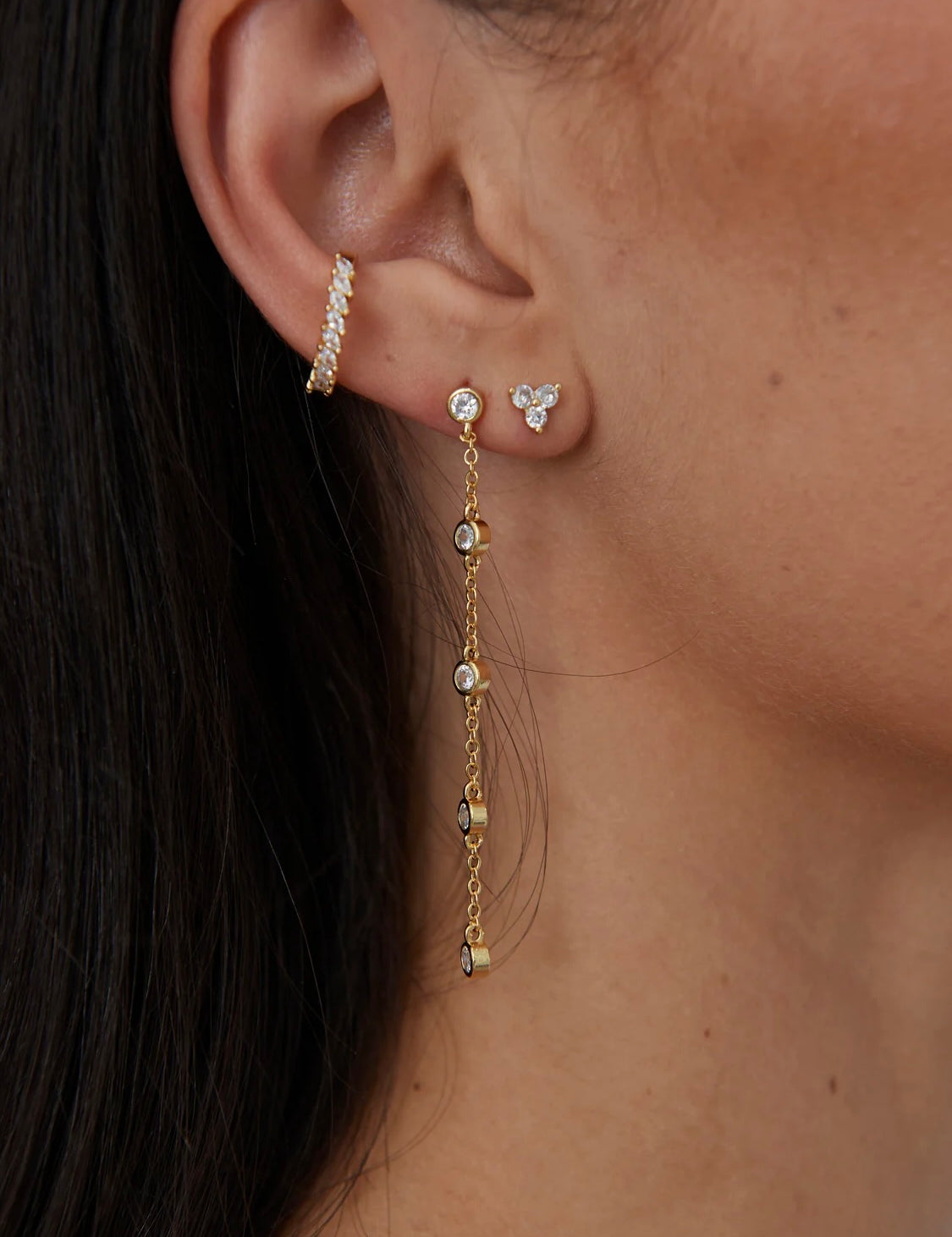 Gold crystal stud earrings with chain drop detail worn on ear
