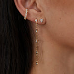 Gold crystal stud earrings with chain drop detail worn on ear