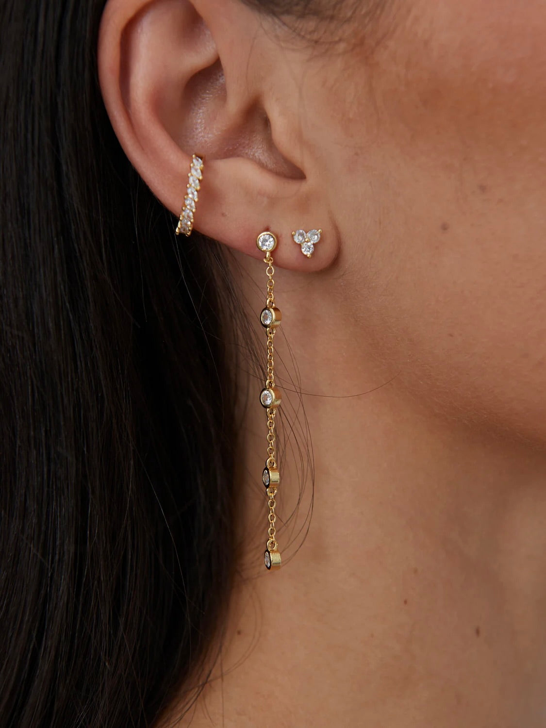 Gold crystal stud earrings with chain drop detail worn on ear