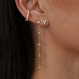 Gold crystal stud earrings with chain drop detail worn on ear
