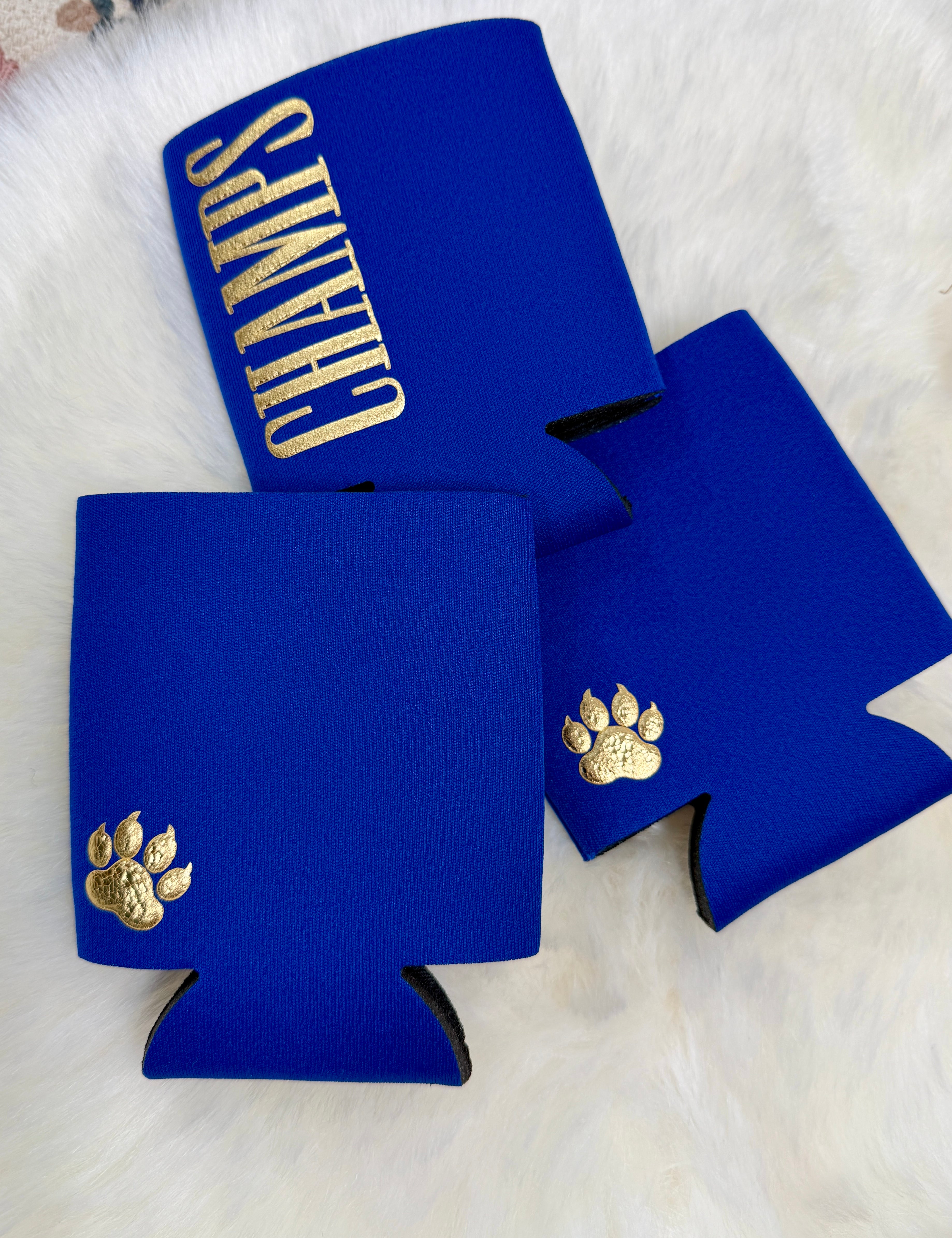 Royal blue neoprene koozies with gold paw print and CHAMPS lettering on white fur background