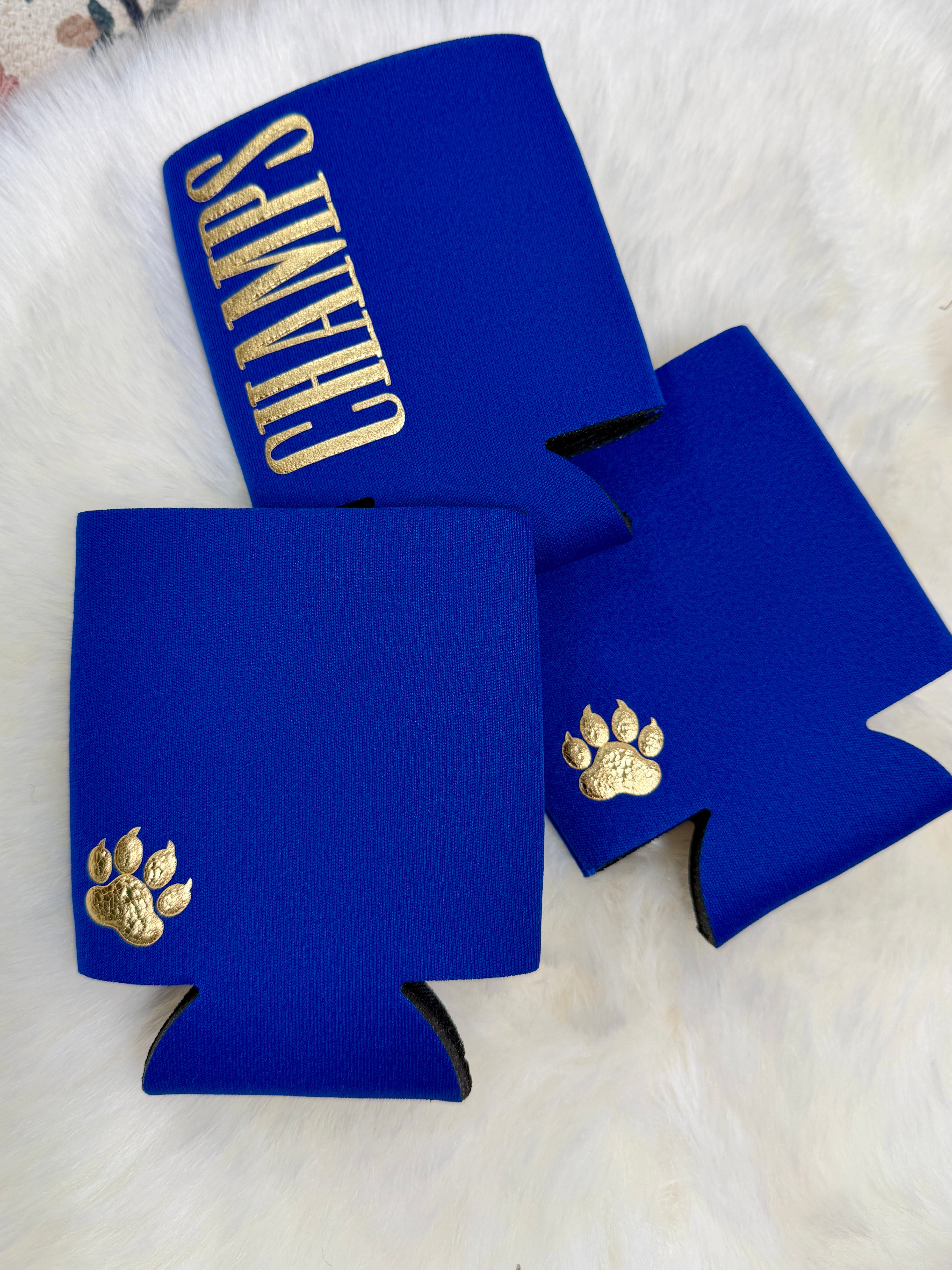 Royal blue neoprene koozies with gold paw print and CHAMPS lettering on white fur background