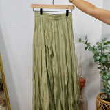 Olive green crinkled midi skirt with elastic waistband displayed on a wooden hanger against a white wall.