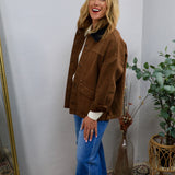 Brown canvas barn jacket with dark collar, styled over white top and blue flare jeans, oversized fit.