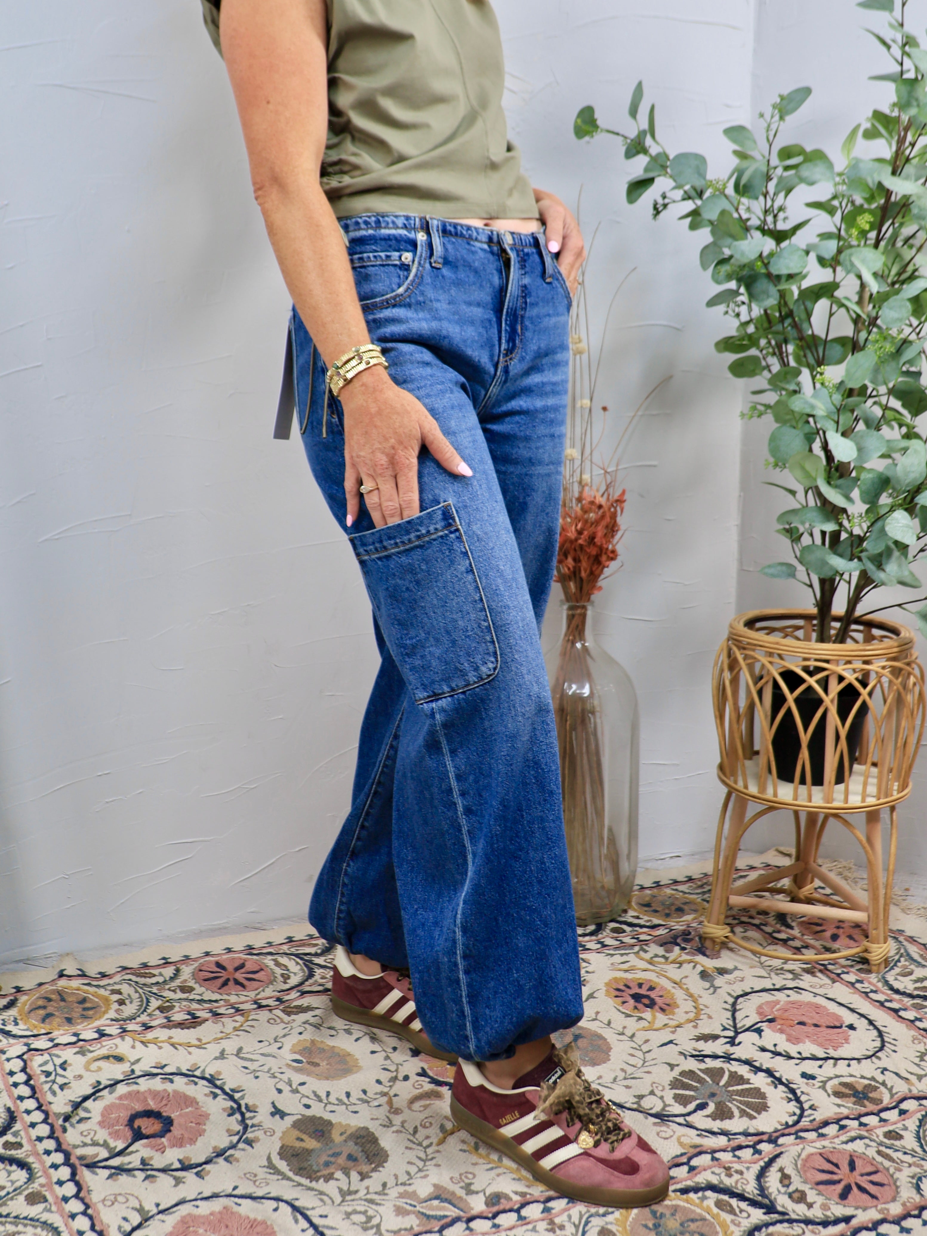 Woman wearing medium blue wide leg cargo denim jeans with olive green tee and burgundy sneakers