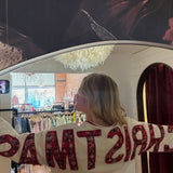 White "Merry Christmas" crewneck sweatshirt with red plaid lettering, shown from back in boutique mirror reflection.