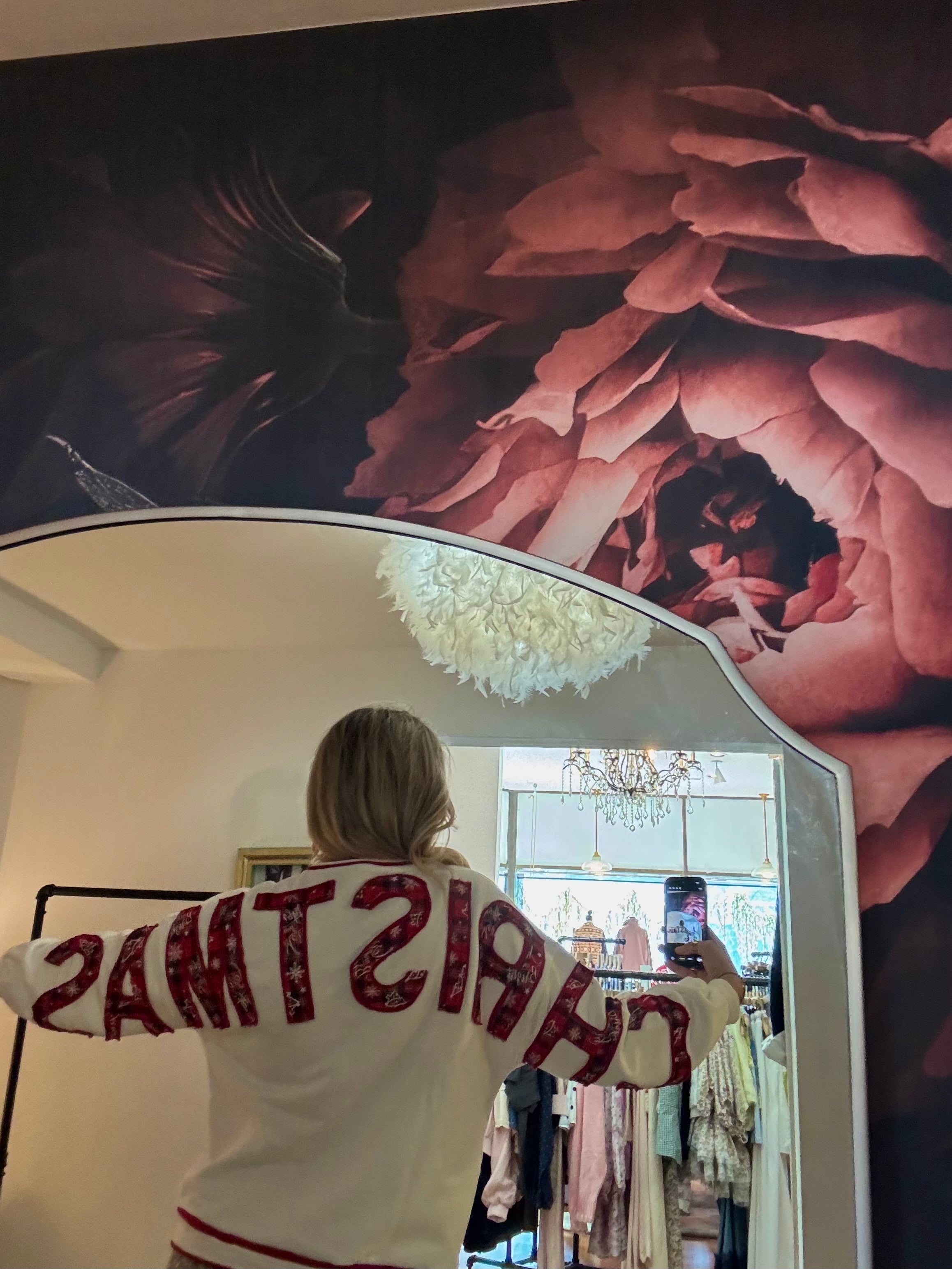 White "Christmas" crewneck sweatshirt with red festive lettering, shown from the back in a boutique mirror selfie.