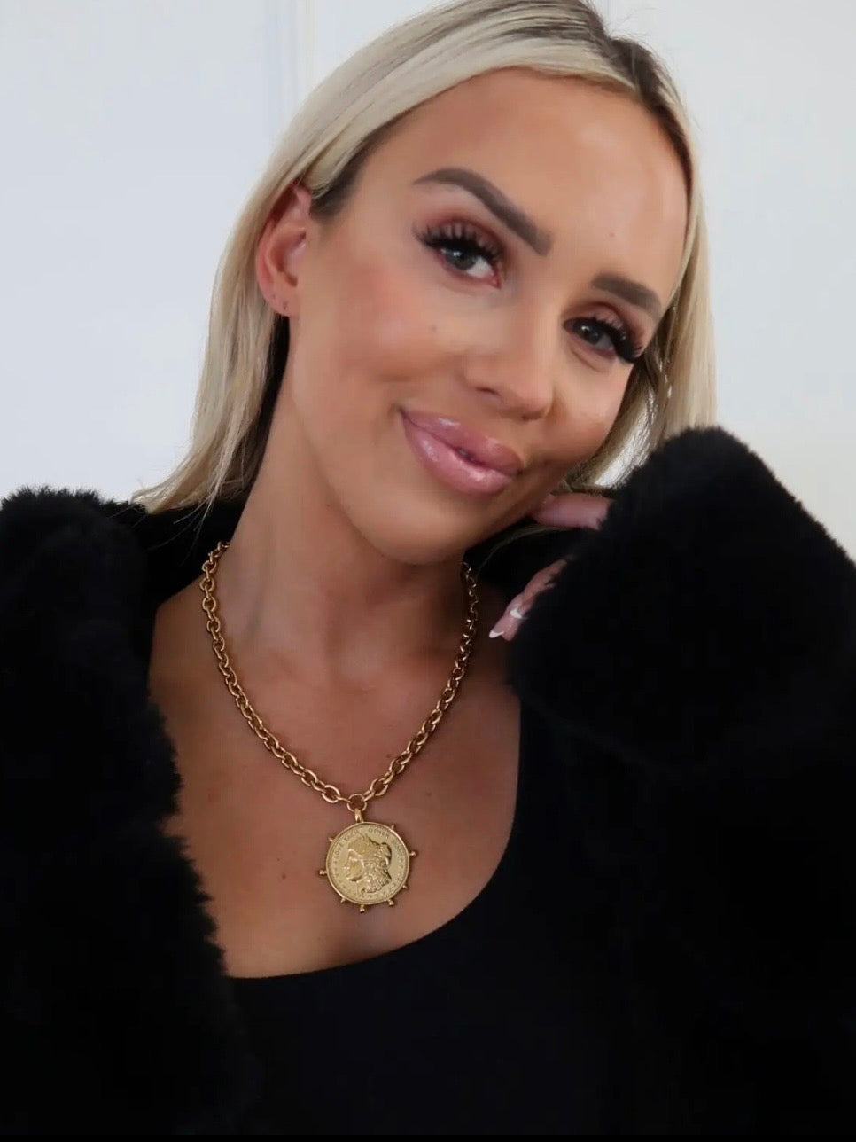Gold chunky chain necklace with vintage coin pendant styled on woman in black outfit