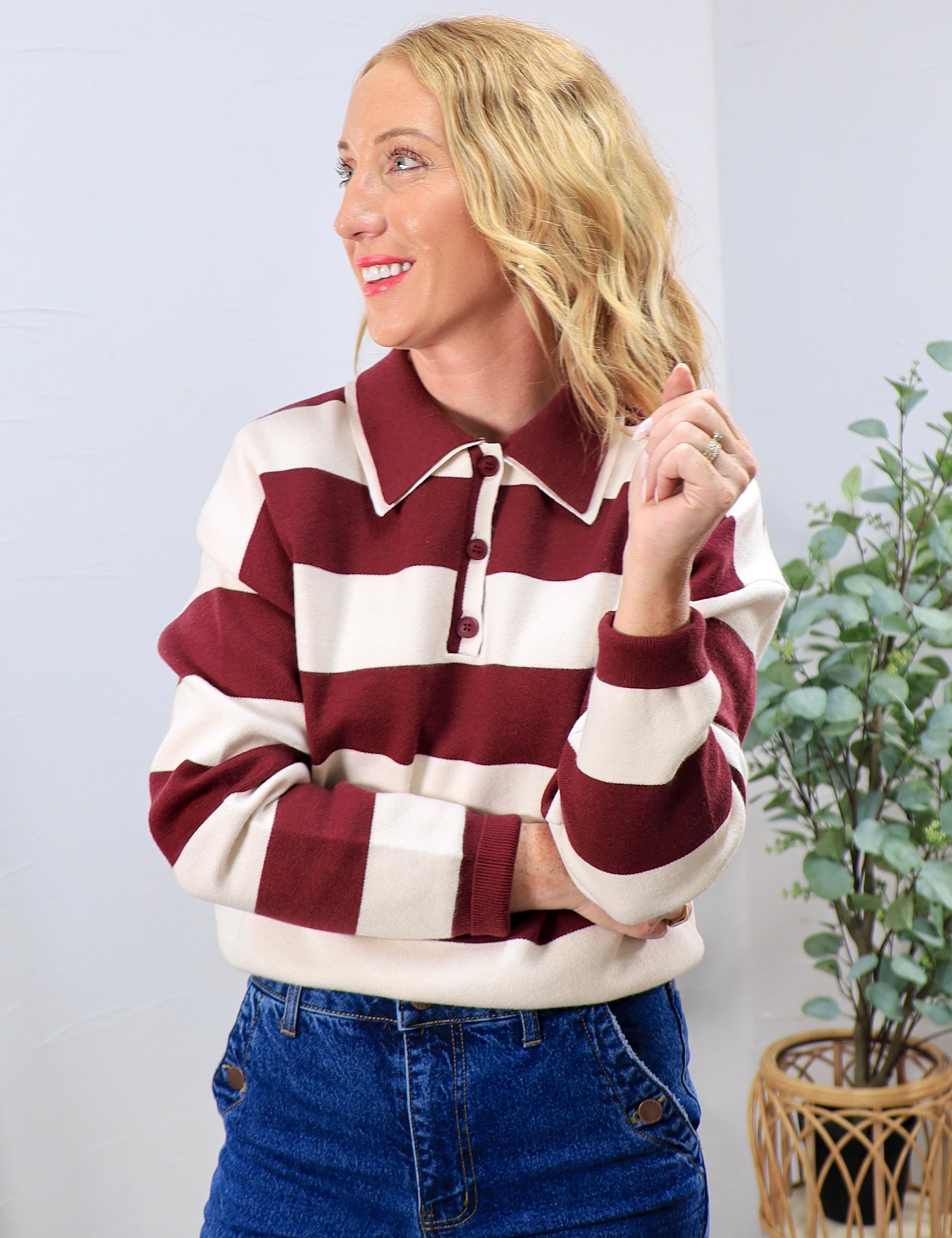 Woman wearing burgundy and cream striped rugby polo sweater top with blue denim jeans