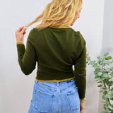 Olive green cropped cardigan with mustard trim detailing, worn over light wash blue jeans, back view.