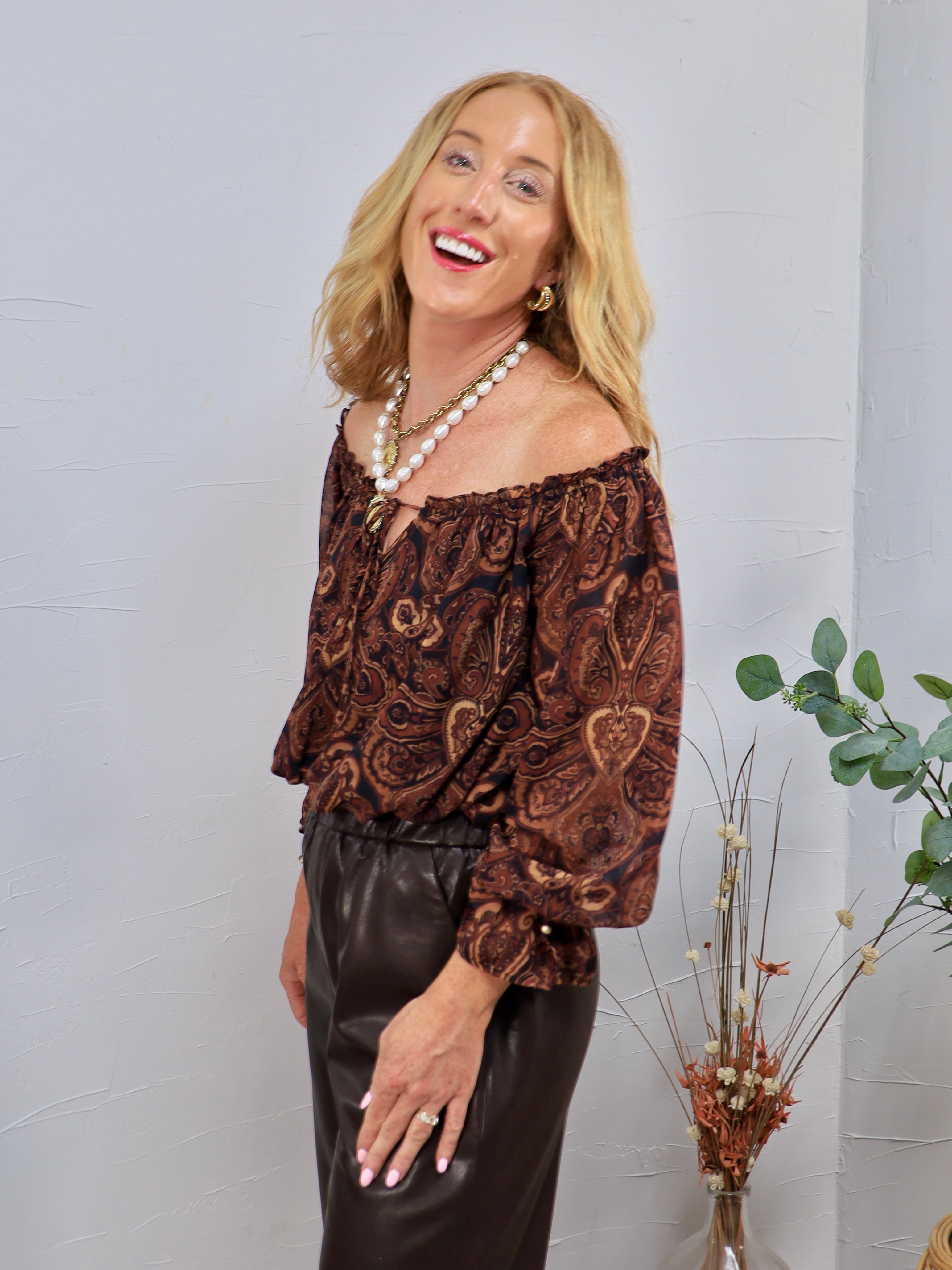 Brown and black paisley off-shoulder blouse with ruffled neckline, balloon sleeves, styled with dark leather pants.