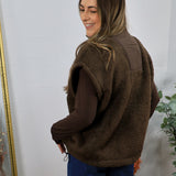 Brown shearling fleece vest with smooth sleeves, worn over dark jeans, side drawstring detail visible.