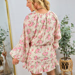 Woman wearing cream floral blouse with pink roses, long sleeves, and ruffled hem, styled with white boots in boho interior se