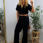 Woman wearing black short-sleeve coveralls with brown studded belt and yellow boots, styled with blonde hair in bohemian inte