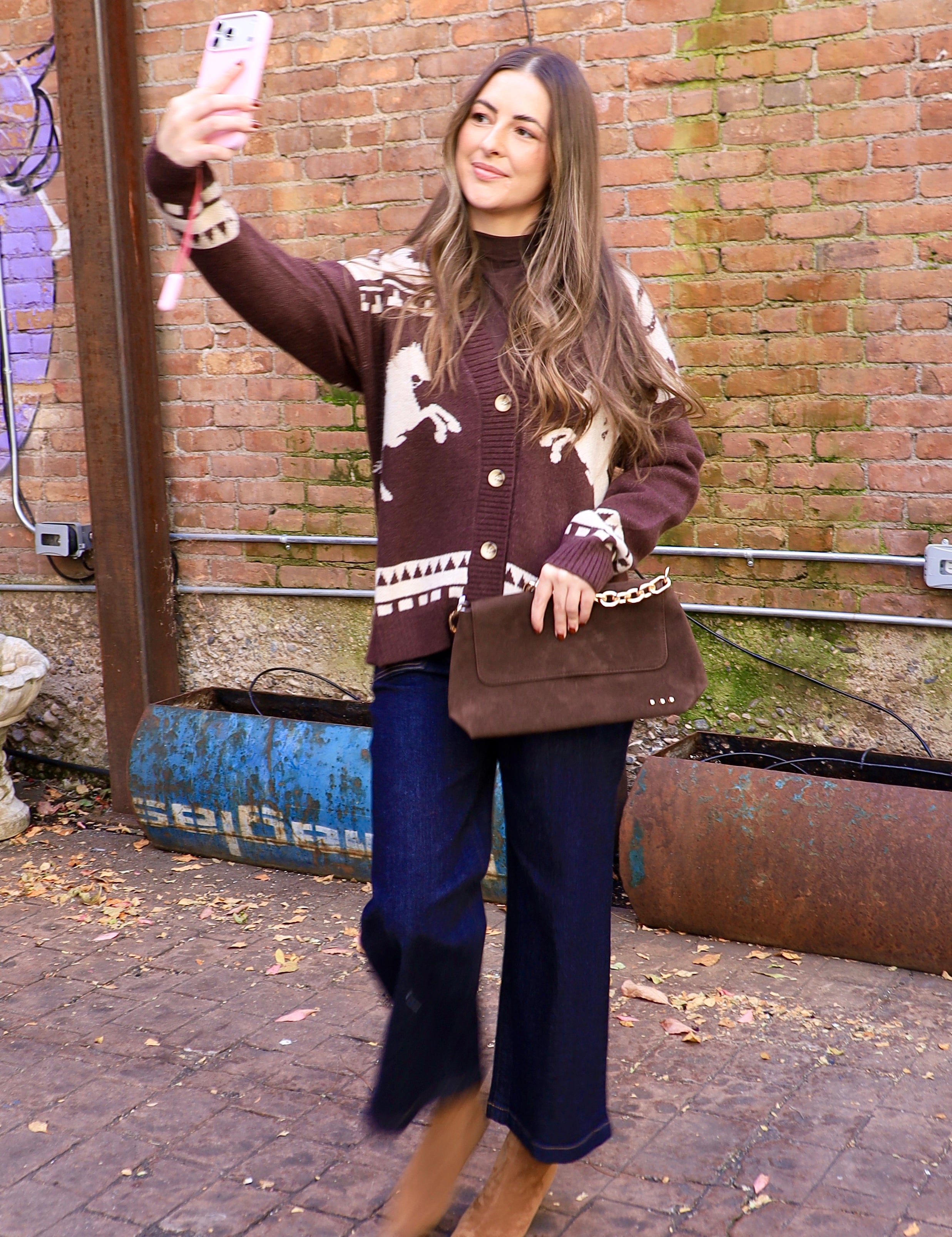 Woman wearing chocolate brown horse-print cardigan with dark wide-leg jeans and brown suede boots