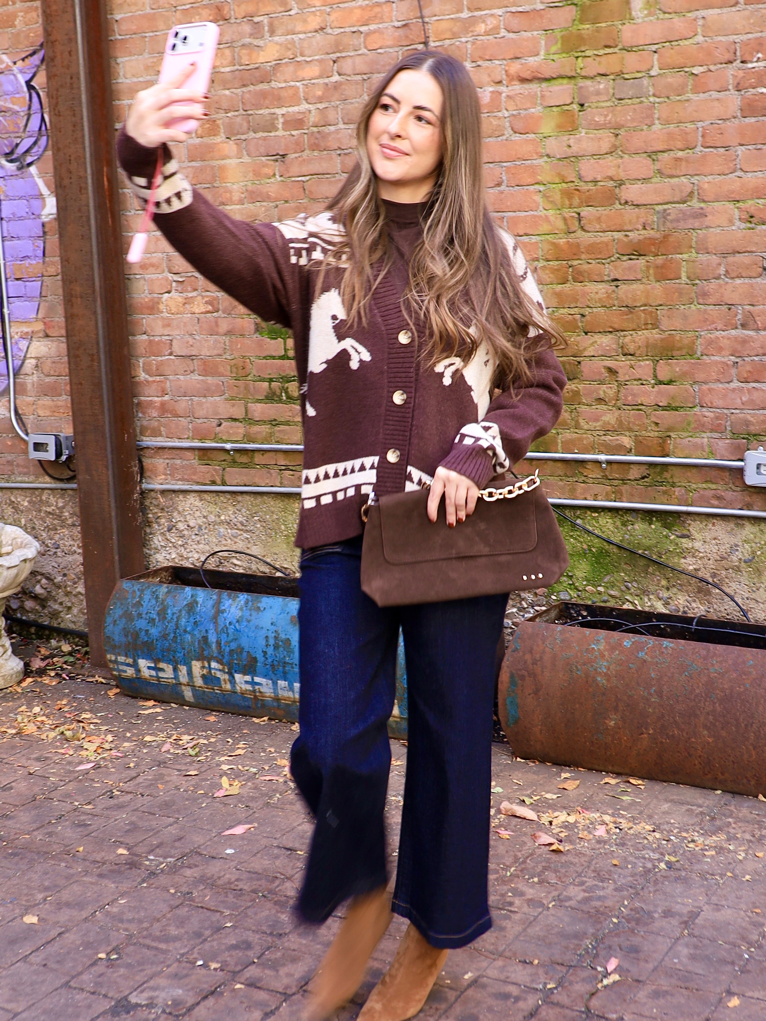 Woman wearing chocolate brown horse-print cardigan with dark wide-leg jeans and brown suede boots