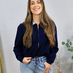 Navy zip-up cardigan with contrast blue collar, worn over a striped shirt with light wash jeans.