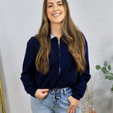 Navy zip-up cardigan with contrast blue collar, worn over a striped shirt with light wash jeans.