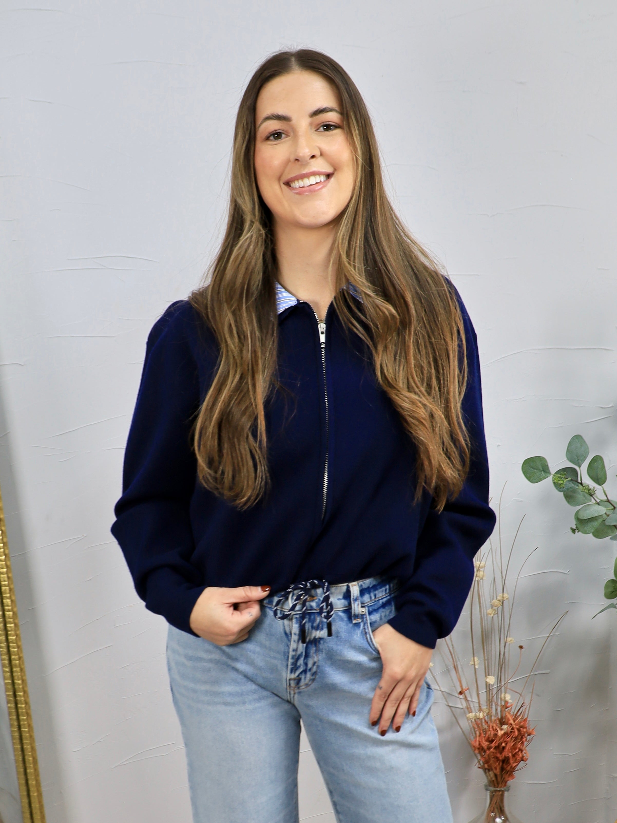Navy zip-up cardigan with contrast blue collar, worn over a striped shirt with light wash jeans.